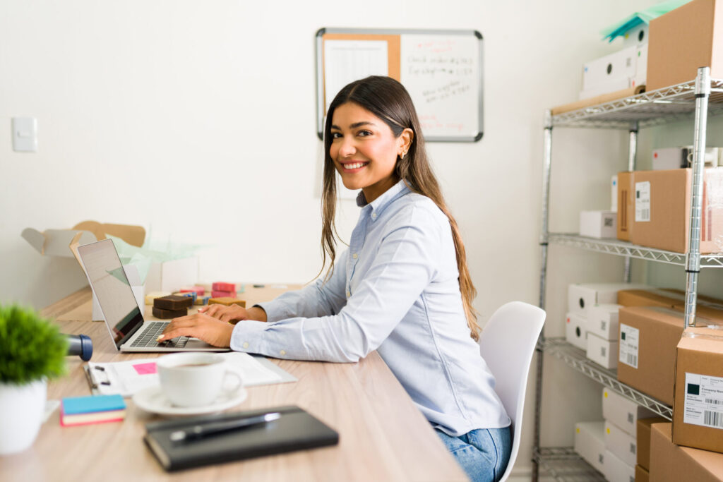 uma mulher sorrindo para a foto enquanto digita no notebook.