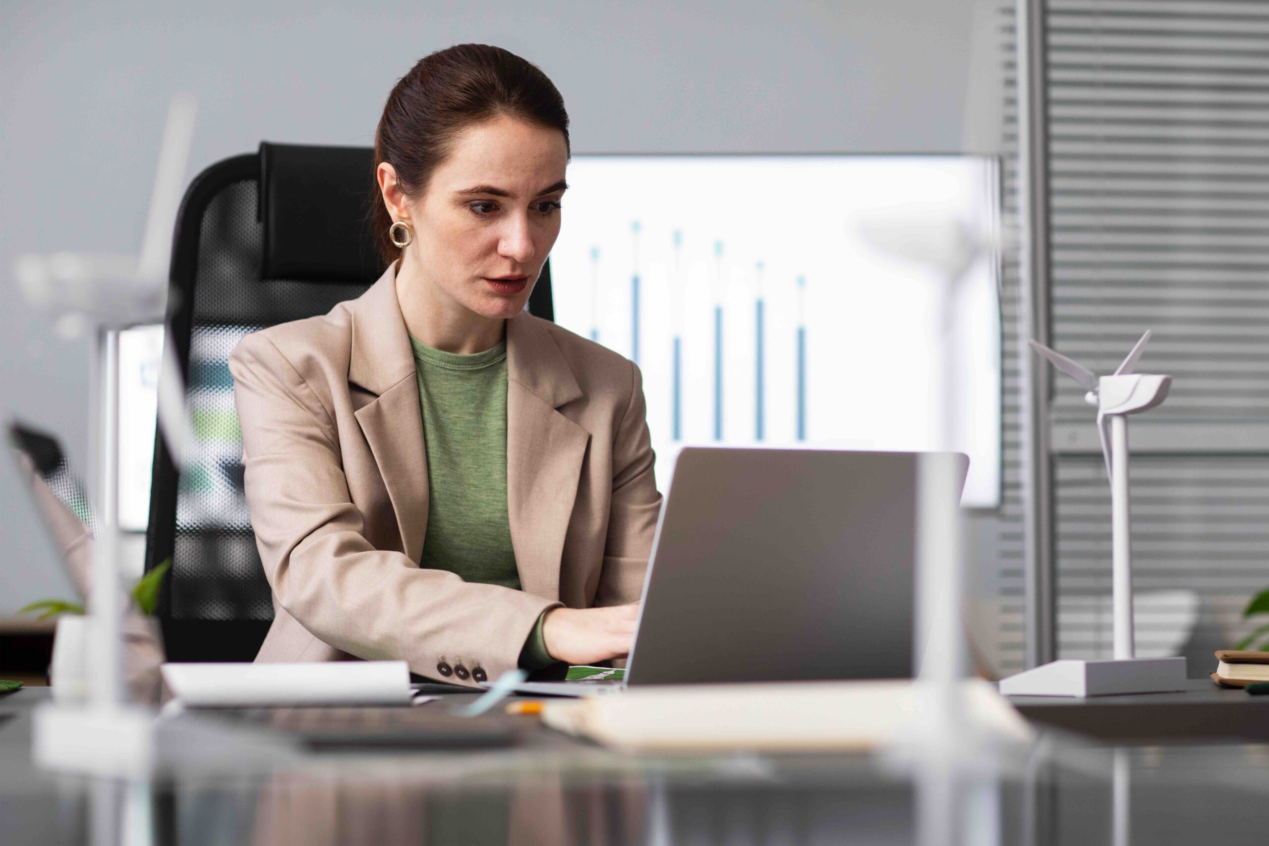 A imagem mostra uma mulher, executiva, em um escritório enquanto mexe no notebook.